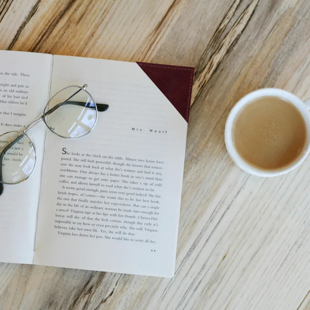 Open book with glasses on a wooden surface next to a cup of coffee