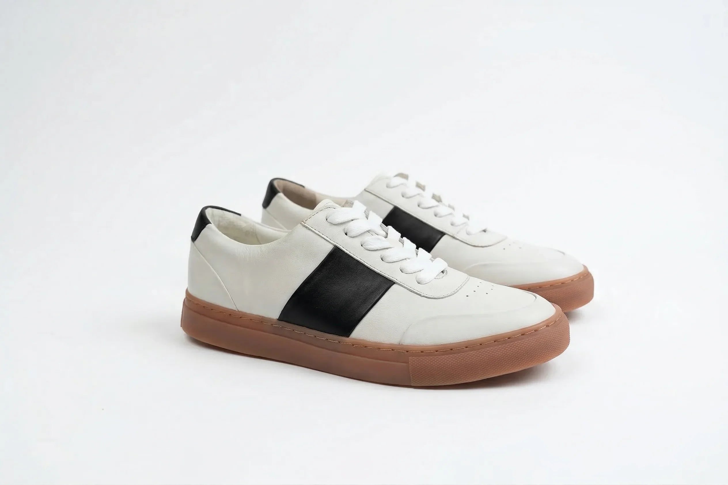 White leather sneakers with black stripe and brown sole on white background