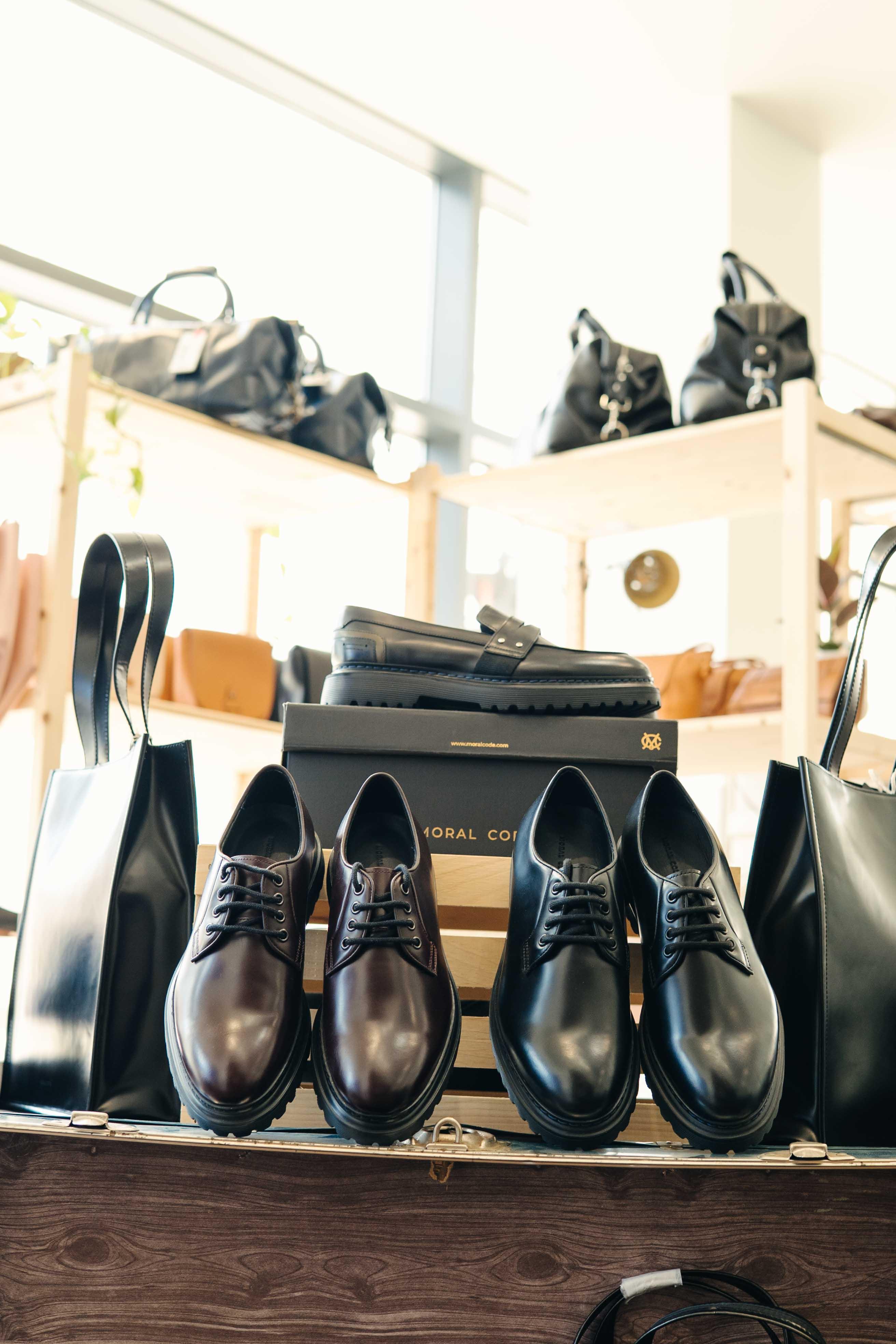 Premium leather dress shoes and loafers displayed with black leather bags in a modern store
