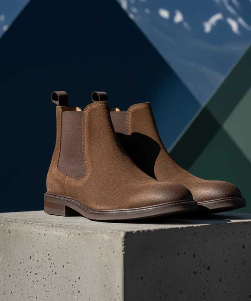 Men's brown suede Chelsea boots with elastic sides on a concrete pedestal
