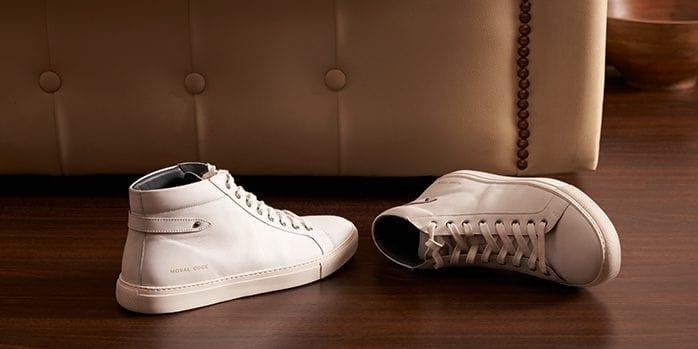 White leather sneakers on wooden floor with beige tufted sofa background