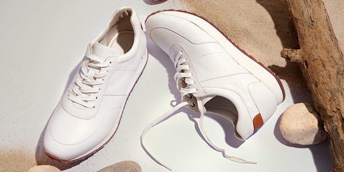 White leather sneakers on sand with natural wood and stones, stylish men's footwear