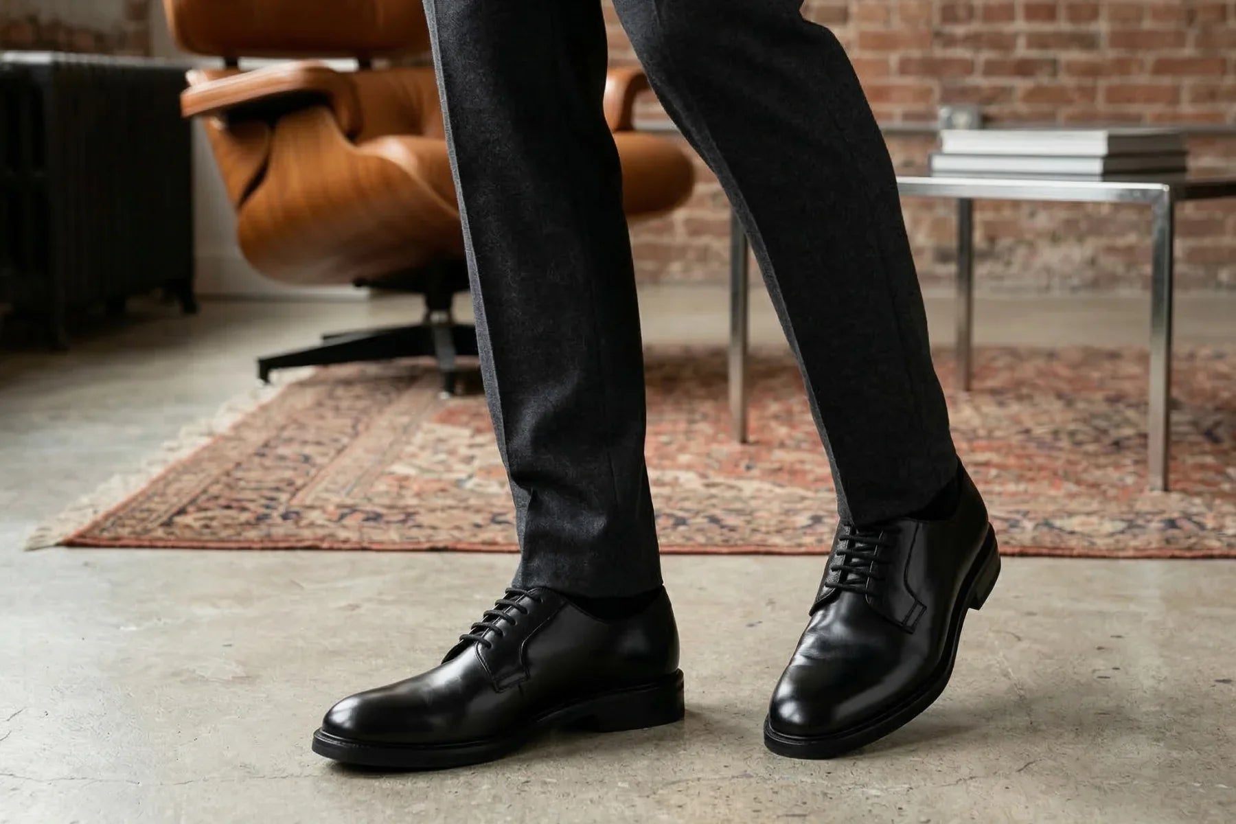 Classic black leather dress shoes on a man in dark trousers in a stylish living room setting  