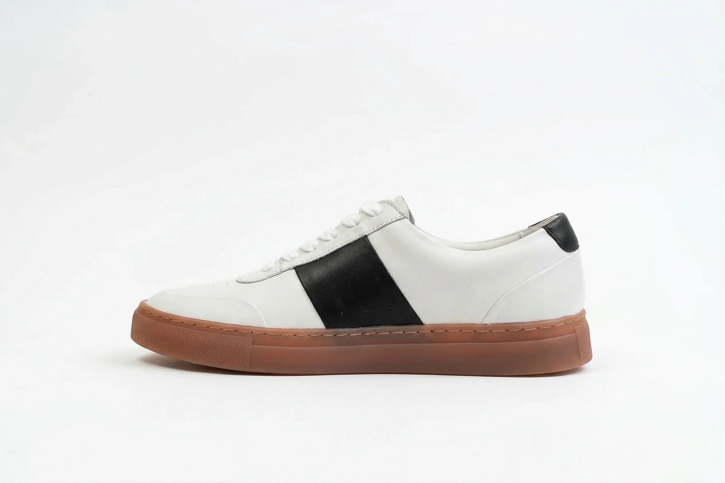White leather sneaker with black accents and brown rubber sole on white background 