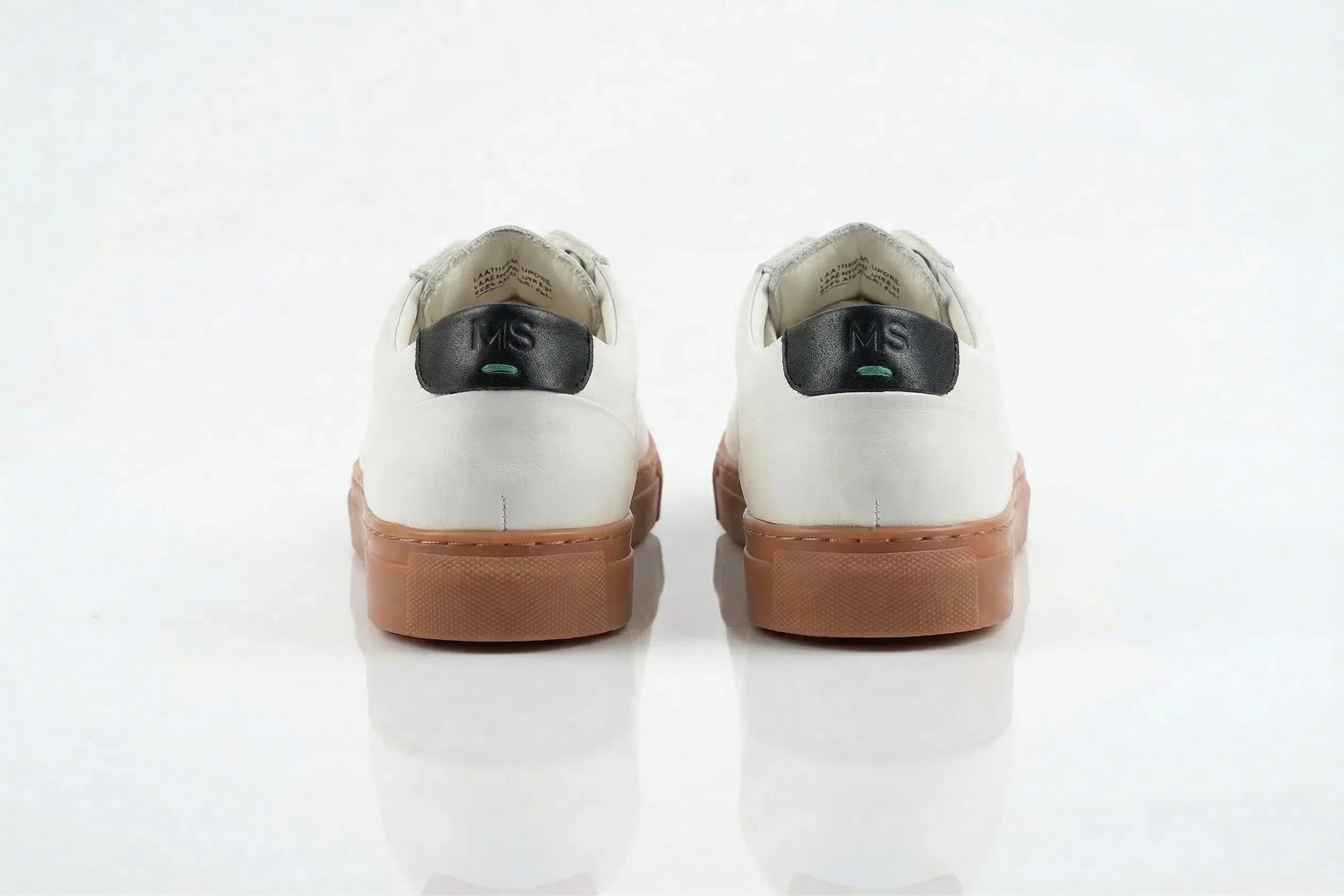 Back view of white leather sneakers with tan soles and black heel tab, on white background 