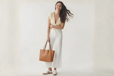 Woman wearing white pants, cream blouse, white leather loafers, and holding a tan leather tote bag 