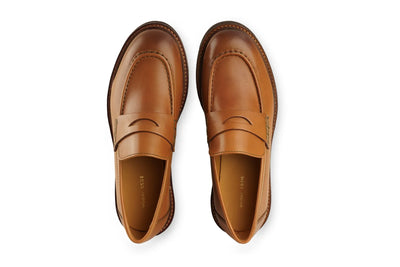 Pair of men's cognac leather penny loafers with stitched detailing, top view on white background 